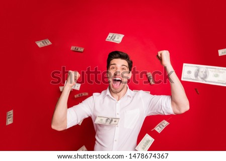 Photo of wealthy rejoicing overjoyed man standing in rain of dollar banknotes while isolated with red background