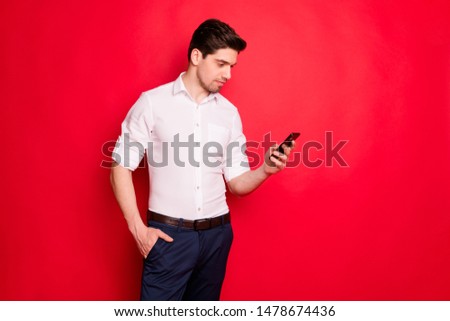 Photo of attractive man staring at telephone in search of something interesting while isolated with red background