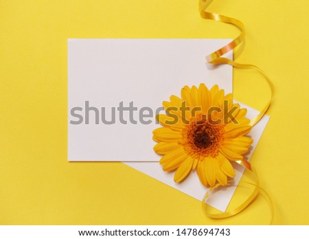 Yellow background with white blank paper and flower. Creative concept.