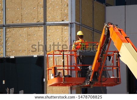 A construction worker, working at heights is harnessed to his sky lift and wearing safety gear. He is using a high speed grinder with a cutting wheel to cut an access panel in a metal plate. Royalty-Free Stock Photo #1478708825