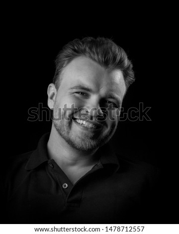 young hipster man smiles with all his teeth. The guy is cheerful and positivny on a dark background. black and white. bw.