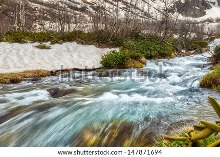 View to snow on Caucasus mountains over motion blurred stream near Arkhyz, Karachay-Cherkessia, Russia