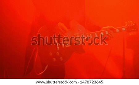 Close up shot of man playing guitar on concert stage. Smoke, red light. Entertainment and art concept