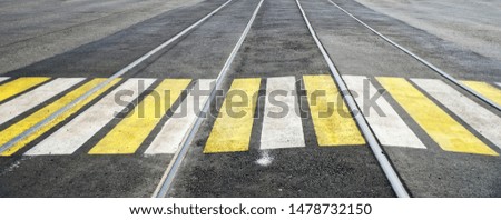 Paved crosswalk over tram rails, marked with white and yellow paint. Road safety. Urban economy.                              