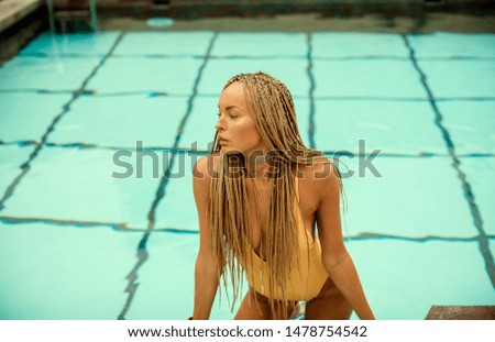 fashion outdoor photo of beautiful girl with blond hair in luxurious swimming suit relaxing in swimming pool
