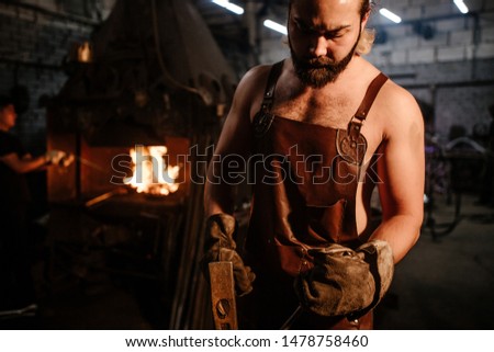 Blacksmith forges iron on the anvil with a hammer on the background of a hot furnace for the forge