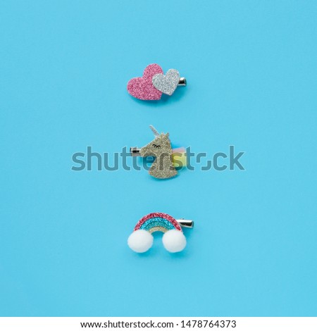 Set of children's shiny hair clips in the form of a unicorn, rainbow and hearts on a blue background.