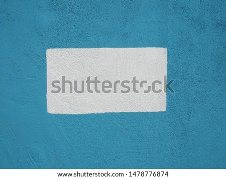 Blue background with a white rectangle in the middle. Painted wall with a geometric figure.