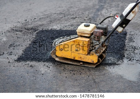 Asphalt vibratory plate compactor. Pothole repair process. Asphalt tamping machine. Pothole patching and repair. Laying asphalt around the hatch. New asphalt Royalty-Free Stock Photo #1478781146