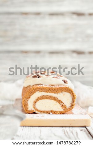 Beautiful fresh baked pumpkin spice roll cake with powdered sugar, pecans, cream cheese filling and icing. Extreme selective focus with blurred background.