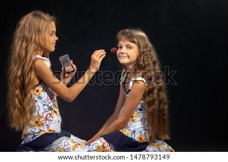 The older sister is applying powder to the younger girl's face
