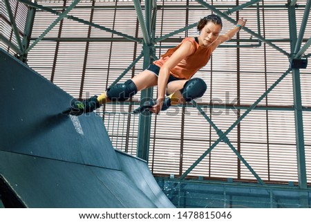 Rollerblader jump high from big air ramp performing trick. Indoors skate park equipment.