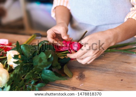 close up cropped photo of female florist making bunch and tying ribbon at flower shop.