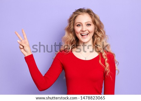 beautiful charming happy girl gesturing v-sign with two fingers looking at camera isolated on blue background. Advertisement concept. victory sign. isolated blue background, studio shot