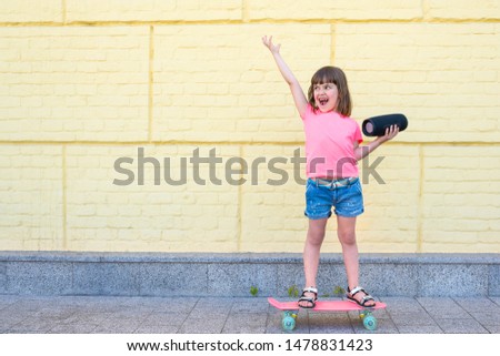 Cute little girl with a skateboard listening to music on a background of a yellow brick wall. Child, hipster.