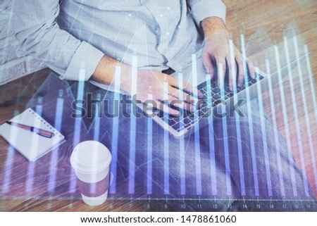 Double exposure of graph with man typing on computer in office on background. Concept of hard work.