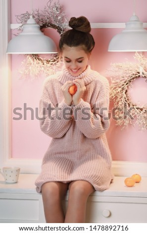 Young smiling woman with dark hair sitting in cozy kitchen and holding tangerines. Winter time, coziness concept, new year eve, christmas. Close up portrait