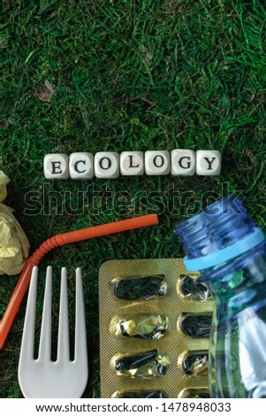 Ecology word written on wood block on a background of green moss. Scattered trash. Ecological problem. Save the planet
