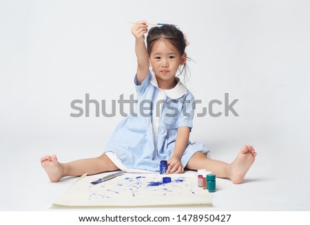 Little Asian Girl is painting by brush on white paper drawing in uniform of kindergarten school, she so very happy with her activities 