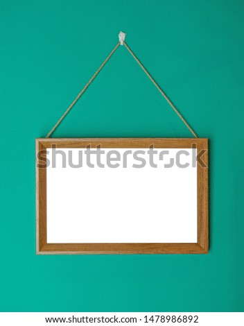 White picture in wooden square frame hanging on the green wall. have space for put text and picture.