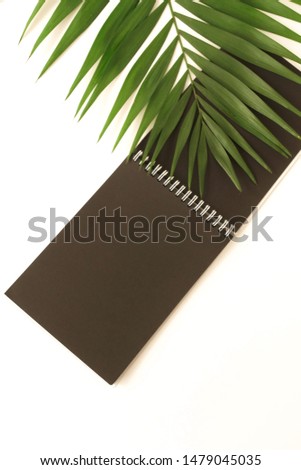 black notebook mock up and green palm leaf on a white background top view. Copy space.Flat lay minimal composition.