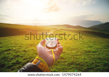 Male hand with a magnetic compass ea against the backdrop of a beautiful landscape at sunset. The concept of navigating the search for your own path and orientation to the cardinal points Royalty-Free Stock Photo #1479074264