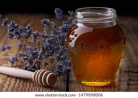 Honey in a glass jar, a spoon for honey, lavender flowers on an old wooden table. Dark background.