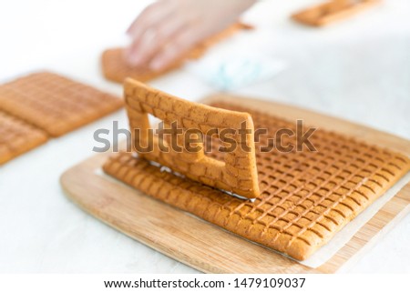 Preparation for Christmas, New Year. Cooking and decoration of traditional advent gingerbread house, female hands in picture, top view, white background.