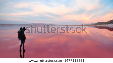 Silhouette of photographer takes a photo at amazing sunset with reflected  waters of Maharlu pink lake at sunset - Shiraz, Iran