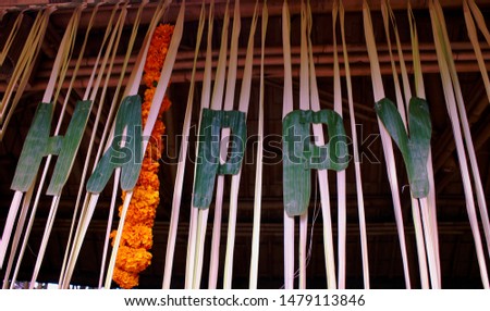 "HAPPY" spelt out in lettering cut from banana leaf, hanging next to a garland of marigold flowers, Ubud, Bali, Indonesia.