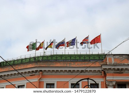 Waving national flags of different countries on flagpoles on the roof of the house in overcast day. Seven fluttering flags