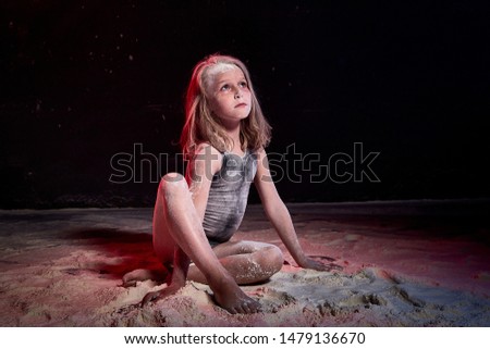 Small blonde girl during photoshoot with flour in dark studio