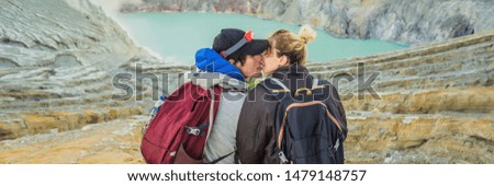 BANNER, LONG FORMAT Young tourist man and woman sit at the edge of the crater of the Ijen volcano or Kawah Ijen on the Indonesian language. Famous volcano containing the biggest in the world acid lake