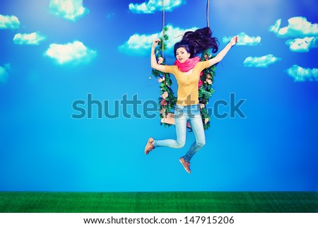 Pretty girl is swinging on a swing over blue sky.