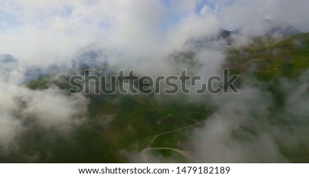 drone aerial view flying above the clouds around a beautiful green mountain scenary