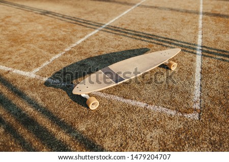 Longboard on old tennis floor. Longboard stands on a brown background. Background. Closeup photo of one skateboard and artificial turf cover.Longboarding concept. Copy space