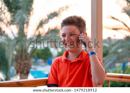 Portrait smiling teenager boy talking on the phone, Cute kid talking on his mobile phone with the sunset and palm trees in background