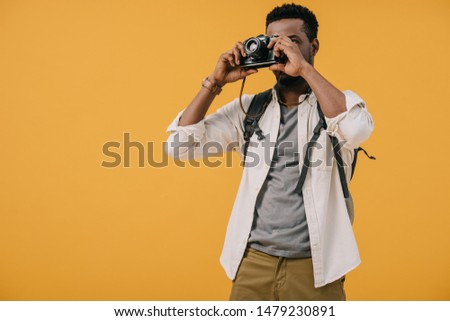 african american photographer covering face with digital camera isolated on orange