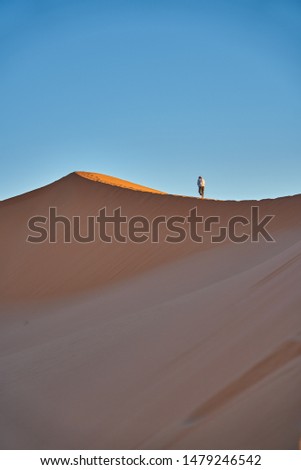 Man is walking up to a sand hill in the desert before sunrise and leaving foot steps. Desert landscape photo was taken in Erg Chebbi near Merzouga, Saharan Morocco.