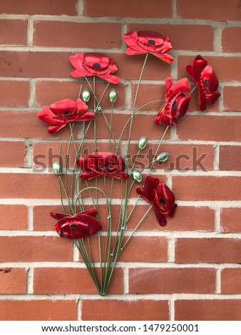 Metal poppy house decoration against a classic red brick wall.