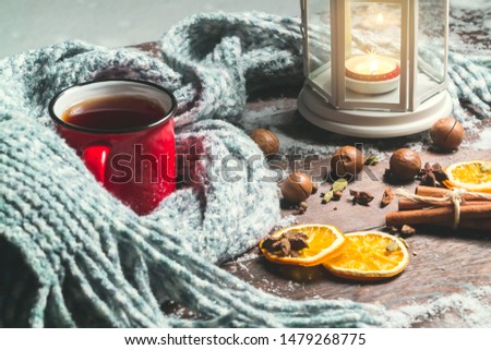 Lantern with a burning candle, spices and a red mug with hot coffee on a snowy wooden table
