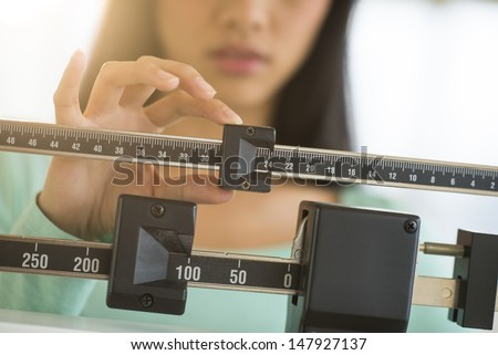 Midsection of mid adult Asian woman adjusting balance weight scale Royalty-Free Stock Photo #147927137