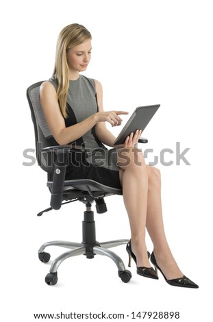 Full length of young businesswoman using digital tablet while sitting on office chair against white background