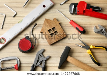 Composition with house figure and repair tools on wooden table, above view