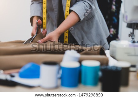Dressmaker cutting dress fabric on sketch line with colorful thread foreground. Fashion designer tailor or sewer in workshop studio designing new collection clothes. Business owner and entrepreneur

