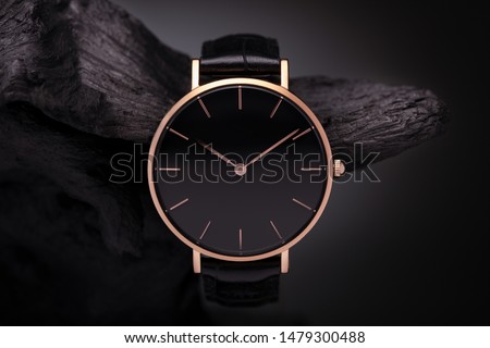 
A luxury gold watch with a black dial. A watch on a beautiful stand, on a beautiful lightly lit gray background. Woman/Man fashion Royalty-Free Stock Photo #1479300488