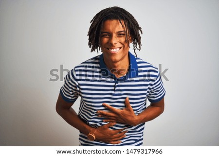Afro man with dreadlocks wearing striped blue polo standing over isolated white background smiling and laughing hard out loud because funny crazy joke with hands on body.