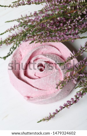 Pink marshmallows in the form of a flower in icing sugar. Lies on white painted boards. Nearby lies a bouquet of fresh heather. View from above.