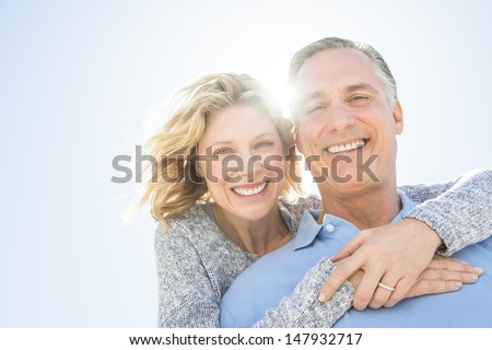 Low angle portrait of cheerful mature woman embracing man from behind against clear sky Royalty-Free Stock Photo #147932717