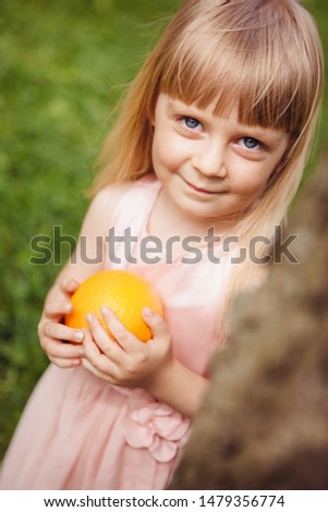 Little girl with orange fruit smile outdoors in park in summer